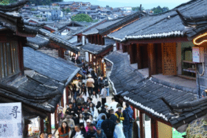 Crowded street in a traditional Chinese town with timber storefronts and tiled roofs, shoppers browse along a narrow lane.